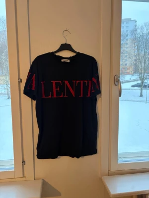 Svart t-shirt från Valentino - Cool svart t-shirt från Valentino med stort rött tryck över bröstet och ärmarna. Klassisk rund hals och korta ärmar. Perfekt för dig som gillar statement-plagg och exklusiva märken.