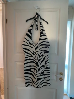 Zebramönstrad halterneckklänning Gina Tricot - Säljer en zebramönstrad kort halterneckklänning från Gina Tricot. Klänningen har svartvitt mönster, djup urringning och knyt i nacken. Perfekt för dig som vill sticka ut med en trendig look.