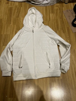 Vit quiltad jacka  - Säljer en stilren vit hoodie med quiltat mönster på fram- och baksidan. Hoodien har dragkedja framtill, två fickor med dragkedja och ribbade muddar vid ärmslut och nederkant. Perfekt för dig som gillar en clean och modern look.