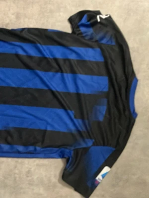 Inter Milan matchtröja Nike blå/svart - Säljer en Inter Milan matchtröja från Nike i blått och svart med klassiska vertikala ränder. Tröjan har korta ärmar, guldfärgade detaljer och Paramount+ som sponsortryck på bröstet. Perfekt för dig som älskar fotboll och vill bära ditt lag.