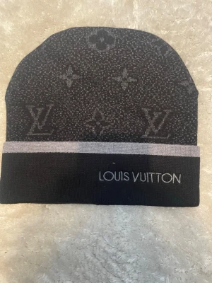 Svart mössa från Zara - Snygg svart mössa från Zara med klassiskt monogrammönster och grå kant. Märkets logga är broderad framtill och insidan har en blå etikett med  Perfekt accessoar för dig som gillar exklusiv streetstyle.