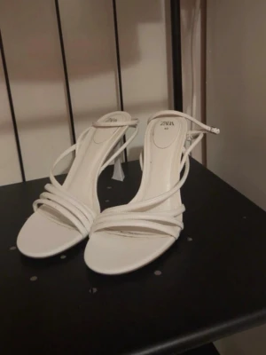 Vita strappy pumps från Zara - Säljer ett par vita pumps från Zara med tunna remmar. Skorna har en elegant klack och öppen design, perfekta för att lyfta vilken outfit som helst.  Klacken är 9 cm. 