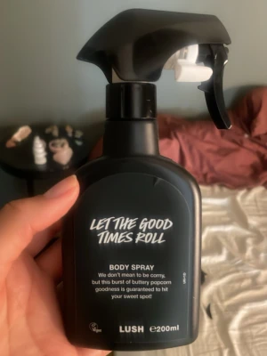 LUSH Let The Good Times Roll Body Spray - LUSH Let The Good Times Roll Body Spray i svart plastflaska med spraymunstycke. Doften har inslag av smörig popcorn och sötma. Flaskan rymmer 200 ml, ungefär lite mer än halva kvar. har en modern, stilren design med vit text på svart bakgrund.