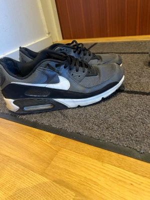 Nike Air Max 90 svartvita sneakers - Svartvita Nike Air Max 90 sneakers med klassisk vit swoosh på sidan och synlig Air Max-dämpning i sulan. Ovandelen är i mesh och läder med svarta skosnören och vit mellansula. Perfekta för dig som gillar sportig och tidlös stil.