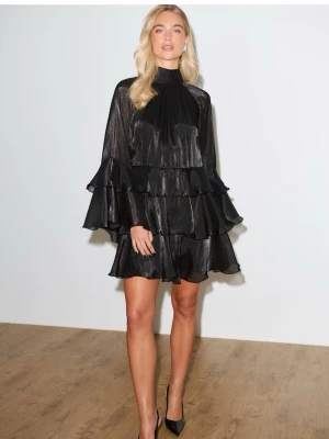 Svart volangklänning med hög krage - Säljer en svart kort klänning med flera volanglager och hög krage. Klänningen har långärmade ärmar och en lös passform. Materialet är glansigt och ger en lyxig känsla. Perfekt för dig som vill sticka ut med en elegant look. Den är precis samma skick som på bilderna, använd endast under ett kalas.