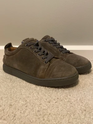 Loubs skor - Snygga sneakers i brun mocka med matchande grå snören och sula. Skorna har en låg profil och klassisk design, perfekt för en clean och stilren look. Insidan är fodrad i ljust material och yttersulan har en röd detalj undertill. OPS har inte kvar lådan!