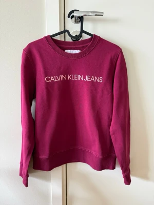 Calvin Klein Jeans fuchsia collagetröja, storlek S - Calvin Klein Jeans fuchsia collagetröja, storlek S  •Snygg rosa/fuchsia bommulströja från Calvin Klein Jeans med vit logotyp framtill.  •Tröjan har rund halsringning, långa ärmar och ribbade muddar vid ärmslut och nederkant. •Perfekt för en trendig och avslappnad look. •Knappt använda, ser ut som ny. Ingenting att anmärka på. Köpte för 1500 kr. Tvättad.  Djur-och rökfritt hem