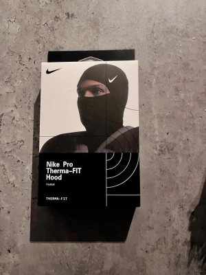Nike skimask  Pro Therma-FIT Hood - Nike Pro Therma-FIT Hood är en svart, tight huva som är designad för att hålla dig varm med Therma-FIT-teknologi. Perfekt för sport och träning, kan bäras under hjälm eller på egen hand. Materialet är mjukt och stretchigt för optimal komfort.