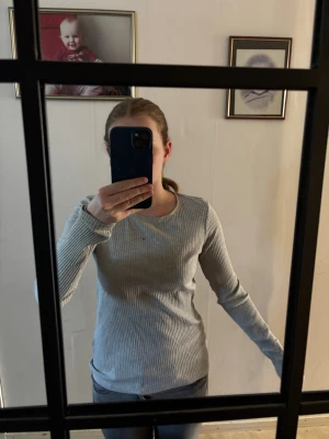 Ljusgrå ribbad långärmad tröja - Säljer en enkel och stilren ljusgrå ribbad långärmad tröja med rund halsringning. Tröjan har en kroppsnära passform och är perfekt för lager på lager. Passar till både jeans och kjol. Finns en liten grå fläck på bröstkorgen som man kan se på bilden 