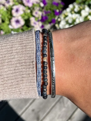 Armbands set  - Säljer ett snyggt set med tre armband: ett med mörkblå och beige pärlor, ett i silverfärgad metall med graverade detaljer och ett blått flätat band. Alla armband går att korrigera i storlek och passar alla storlekar. Perfekt nu till sommaren☀️