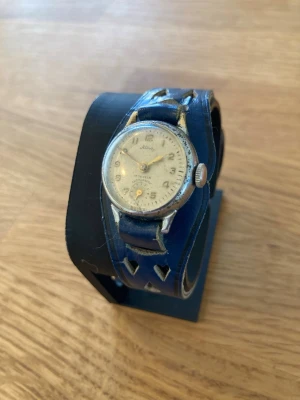 1950 Alira Swiss Mekanisk 17 Jewels 22mm Damur - Schweizisk vintage klocka från Alira, ett mekaniskt armbandsur med 17 juveler och antimagnetisk funktion. Klockan har ett blått läderarmband med utskurna hjärtan. Skick enligt bilder. Säljes otestad.   Värde: 400 SEK Mitt pris: 348 SEK  Skickas snabbt och spårbart. Skriv vid frågor och se gärna mina andra annonser!