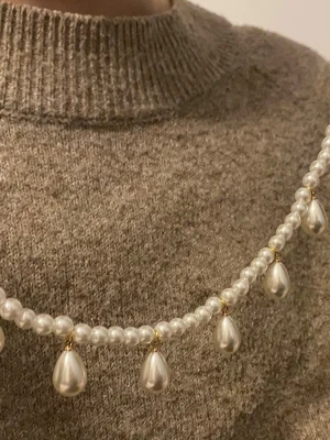 Pärlhalsband med droppformade hängen - Snyggt halsband med vita runda pärlor och droppformade pärlhängen. Halsbandet har små guldfärgade detaljer mellan pärlorna och ger en elegant look. Perfekt accessoar för att lyfta din outfit med en klassisk touch.