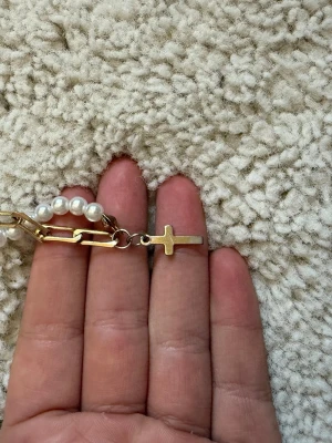 Halsband med pärlor och guldkedja - Unikt halsband med halva kedjan i vita pärlor och andra halvan i guldfärgad metall. Halsbandet har ett litet guldfärgat kors som detalj. Perfekt för dig som gillar att mixa klassiskt och trendigt. Ingen synlig märkning.