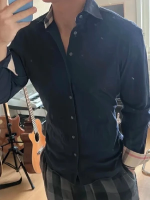 Svart skjorta från Burberry - En skjorta från Burberry. Det är toppen skick på skjortan. använd 2 gånger pga för liten. Om du har fler frågor är det bara att ställa🤝☺️ Skjortan passar garanterat folk i M