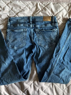 Blå jeans med vit brodyr på bakfickor🫶🏻 - Snygga blå jeans från Gina Tricot med unika vita broderade mönster på bakfickorna. Klassisk femficksmodell med smal passform och normal midja. Perfekta för dig som gillar en cool och avslappnad stil. Supersnygga!🤍