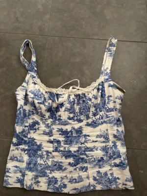 Sommar topp  - Superfin sommartopp med blått och vitt mönster, spetskant och knyt framtill. Köpt för över 500 på Urban outfitters och säljs inte längre🥰 Toppen skick och pris kan diskuteras vid snabbköp! 