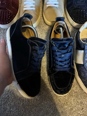 Loubs - Snygga mörkblå sneakers i sammet med matchande blå skosnören och vit sula. Skorna har en klassisk låg profil och en stilren design som passar till många olika outfits. Perfekta för dig som vill sticka ut med en unik textur och färg på dina sneakers.