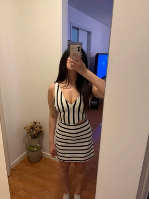 Vit och svart randig kort jm Zara - Snygg kort jumpsuit i vitt med svarta ränder och v-ringning. Klänningen är ärmlös och har en cut-out detalj i midjan som ger en modern look. Perfekt för dig som gillar trendiga och stilrena plagg.