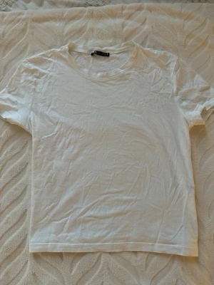 Vit basic t-shirt från Zara - En klassisk vit t-shirt från Zara i mjuk bomull. Modellen är enkel med rund halsringning och korta ärmar, perfekt till alla outfits. Passformen är normal och tyget är tunt och skönt mot huden. Inte använd alls den måste bara strykas annars är den som ny🤗