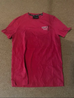 Röd Supply & Demand t-shirt - Röd t-shirt från Supply & Demand med tryck på både bröstet och ryggen. T-shirten har rund hals, korta ärmar och är gjord i mjuk bomull. Stort vitt tryck på ryggen med text och grafisk detalj. Perfekt för en streetwear-look.