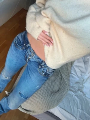 Blå low waist bootcut jeans - Säljer ett par blå low waist jeans med bootcut passform och slitna detaljer på benen. Jeansen har klassiska fem fickor och en cool, avslappnad vibe. Perfekta för dig som gillar en trendig och avslappnad stil. Storlek 26/32🩷