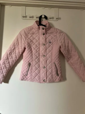 Ljusrosa pufferjacka - Säljer en ljusrosa pufferjacka från Hampton republic  med quiltat mönster, hög krage och silvriga dragkedjor på fickorna. Jackan har tryckknappar framtill och en liten logga på bröstet. Perfekt för kalla dagar när du vill vara både varm och snygg.