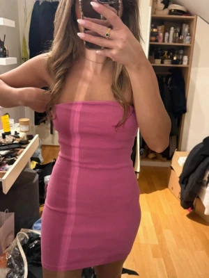 Rosa tubklänning i tight modell - Säljer en rosa, axelbandslös tubklänning i tight passform. Klänningen är kort och har en enkel, stilren design utan synliga detaljer. Perfekt för dig som gillar en minimalistisk look. I strl Large men passar mig som vanligtvis är en strl S