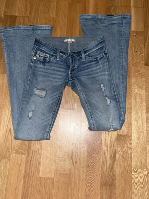 Delulu flair jeans Gina - Snygga ljusblå bootcut jeans från Gina Tricot med slitna detaljer och broderade bakfickor. Jeansen har klassisk femficksdesign, låg midja och är tillverkade i stretchigt denim för en bekväm passform. Perfekta för en avslappnad och trendig look.