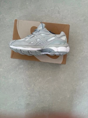 Gråa ASICS sneakers mesh och mocka - Snygga sneakers från ASICS i ljusgrått med detaljer i mesh och mocka. Skorna har en chunky sula och klassisk låg profil. Perfekta för dig som gillar stilrena och sportiga vibes. Loggan syns på sidan och tungan. Skosnören i matchande grå färg.