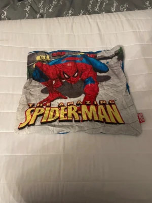 Spiderman kuddfodral Marvel - Säljer ett kuddfodral med Spiderman-motiv från Marvel. Ena sidan har en färgglad bild av Spiderman och texten 'The Amazing Spiderman', andra sidan är blå med svarta spindelnät. Tillverkat i mjukt tyg, perfekt för dig som gillar superhjältar och vill ha något unikt till rummet. Den är 40x40