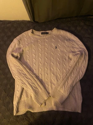 Beige kabelstickad tröja Polo Ralph Lauren - Säljer en vit kabelstickad tröja från Polo Ralph Lauren med klassisk rund halsringning och den ikoniska mörkblå loggan broderad på bröstet. Har bara använt 1 gång och då var den lite stor 
