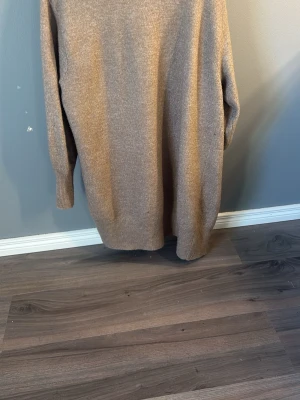 Beige stickad lång tröja - Mysig beige stickad lång tröja med rund hals och långa ärmar. Tröjan har en rak passform och ribbstickade muddar vid ärmslut och nederkant. Perfekt för lager-på-lager och chill dagar.