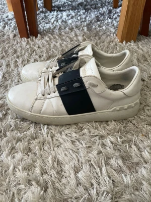 Svarta Valentino Garavani Opens  -  Valentino Garavani med bred svart rem över vristen och ikoniska nitar på hälen. Skorna har klassisk låg profil, vita snören och är tillverkade i läder. Kan släppa dom billigare vid snabb affär. Låda o allt finns