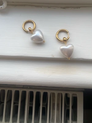 Guldiga örhängen med hjärtformade pärlor - Snygga örhängen med guldfärgade ringar och stora hjärtformade pärlor i vitt. Har bara använt en gång och örhängena är i toppenskick. Man får med påsen och en liten smyckespåse💛💛