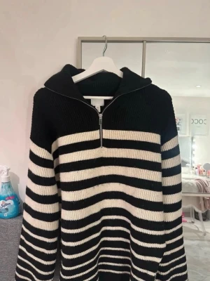 Randig stickad tröja med halv dragkedja - Säljer en svartvit stickad tröja med breda horisontella ränder och halv dragkedja framtill. Tröjan har en hög krage och långa ärmar. Perfekt för dig som gillar en avslappnad och trendig look.