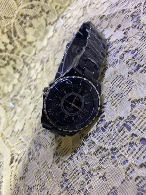 Svart klocka  - Stilren svart klocka med rund urtavla och metallarmband. Klockan har tydliga siffror och markeringar på boetten samt en klassisk länkdesign. Perfekt accessoar för dig som gillar en clean och modern look.