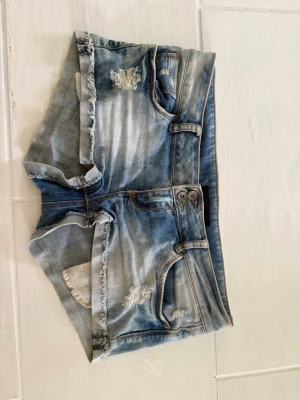 Blå jeansshorts från Tally Weijl - Snygga blå jeansshorts från Tally Weijl med slitna detaljer och fransig kant. Klassisk femficksmodell med knappgylf och ljus tvätt. Perfekta för varma dagar och en avslappnad look.                                                                            Kolla gärna in mina andra annonser, bundle går att ordna för bättre pris!!