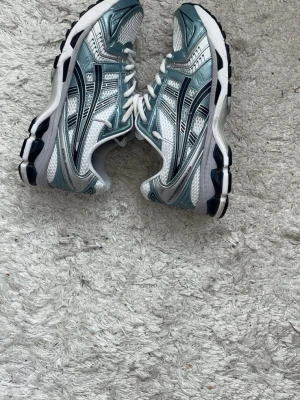 Asics gel kayano - Snygga sneakers från Asics i silver med blå och svarta detaljer. Skorna har vit mesh för bra ventilation, vita skosnören och en rejäl sula med svart och vit färg. Perfekta för dig som gillar sportig och trendig stil.