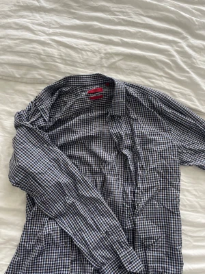 Blårutig skjorta med knappar - Klassisk långärmad skjorta från HUGO BOSS i blått och vitt rutigt mönster. Skjortan har knappar framtill och en klassisk krage. 