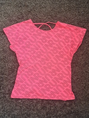 Hot pink topp med RUN-tryck - Snygg hot pink topp med svarta RUN-tryck den. Toppen har korta ärmar och en cool detalj med korsade band över ryggen.