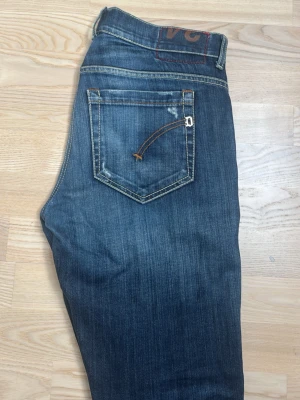 Mörkblå jeans från Dondup  - Snygga mörkblå jeans från Dondup med klassisk femficksdesign och kontrastsömmar. Jeansen har en lätt tvättad look och detaljer som logga på bakfickan och läderpatch i midjan. Perfekta för en avslappnad stil. Skräddarsytt hål i skrevet.
