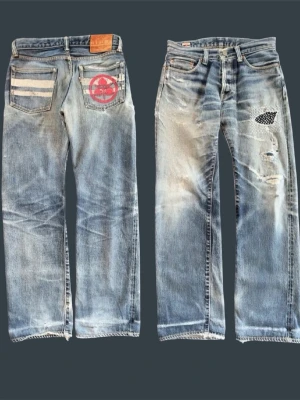 MOMOTARO custom order jeans - Det sjukaste paret Momotaro-jeans du kan hitta på marknaden. Unik custom-design på bakfickorna och handgjord sashiko-lagning på framsidan, vilket ger dem en helt unik karaktär.  Jeansen har redan genomgått flera professionella reparationer. Det finns även några områden med tunnare tyg och mindre hål som ännu inte är lagade, vilket syns på de sista bilderna. Perfekt för den som uppskattar välburna denim med mycket historia och potential för framtida fades och repairs.  Passar ungefär som W29–30. 