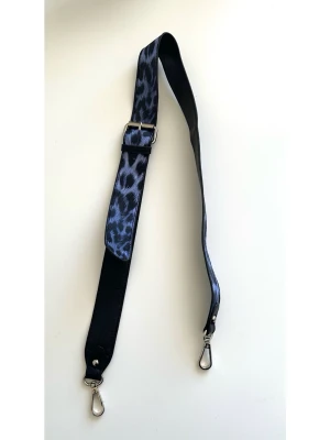 Justerbar axelrem med blå lila leopardmönster - Cool axelrem med leopardmönster i blått / lila och svart. Remmen har silverfärgade spännen i båda ändar för att fästas på en väska. Längden är justerbar med ett spänne i mitten. 98cm lång. Har ett litet skrap på insidan vid ena spännet, se bild, men inget som syns när den används. Är annars i mycket gott skick, som ny!