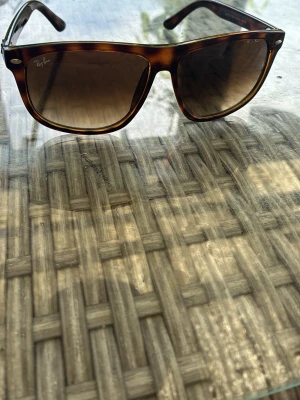 Bruna Wayfarer solglasögon Ray-Ban - Snygga Wayfarer-inspirerade solglasögon från Ray-Ban med brunmelerad båge och mörka glas. Klassisk och tidlös design som passar till allt. Ray-Ban-logga på linsen och sidan av bågen. Perfekta för soliga dagar.