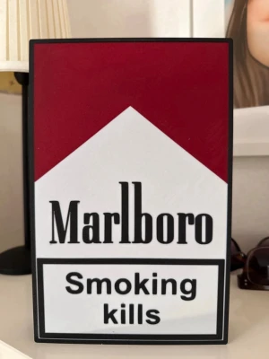 Marlboro LED-skylt röd/vit - Säljer en LED-skylt med Marlboro-logga i rött och vitt. Skylten har texten 'Smoking kills' och lyser upp när den är påslagen. Perfekt som dekoration till rummet eller samlingen. Tillverkad i plast och har en tydlig retrovibe.