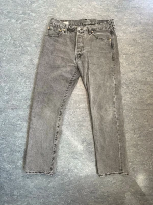 Grå Levi's 501 raka jeans - Säljer ett par klassiska grå Levi’s 501 jeans med rak passform och knappgylf. Något krympta i tvätten, 32/30 är nog en bättre storleksbeskrivning.