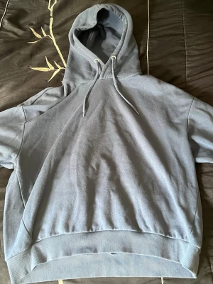 Ljusblå hoodie  - Säljer en ljusblå hoodie med huva från lager. Hoodien har bred mudd i nederkant och är tillverkad i mjukt sweatshirtmaterial. Perfekt för en avslappnad och trendig look. Använt nån gång 