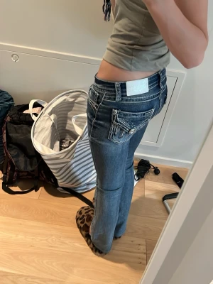Blå bootcut jeans med broderade fickor - Säljer mina favvo blå bootcut jeans med snygga broderade detaljer och dekorationer på bakfickorna💗. Jeansen är köpta i USA och passar till alla typer av kläder. Tillverkade i denim med lätt tvättad look. Perfekta för dig som gillar en avslappnad men trendig stil.