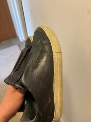 Svarta sneakers från Axel Arigato - Stilrena svarta sneakers från Axel Arigato i slätt läder med vit sula. Diskret guldtext på sidan och minimalistisk design utan synliga snören. Perfekta för en clean och modern look.