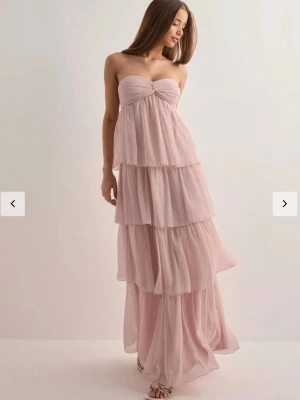 Klänning med volang  - Säljer min fina bandeau volang klänning som är köpt ifrån Nelly☺️Passar till både bal och fest!!  Modellen på klänningen är ”Dreamy Frill Dress” och färgen är ”Light Pink”💕 Använt den endast en gång så den är som ny! Nypris 700 kr
